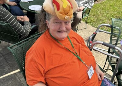 A woman wears a fabric hot dog on her head at an outdoor picnic